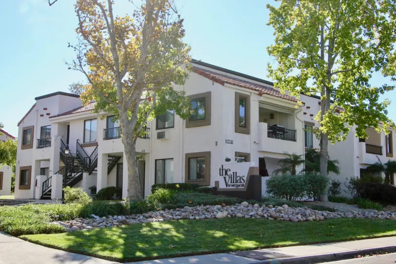 Two story residential building with lush green yard and trees at Villas as New Salem in Mira Mesa California