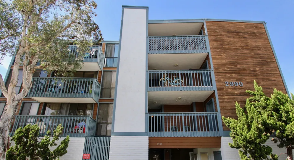 A sunny day including front view of three story apartment in 2290 Mission with trees and bycyle