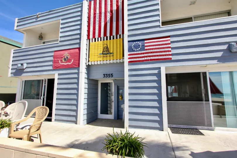 The exterior of a four unit apartment building with flags displayed and lawn furniture at MB Townhomes complex.