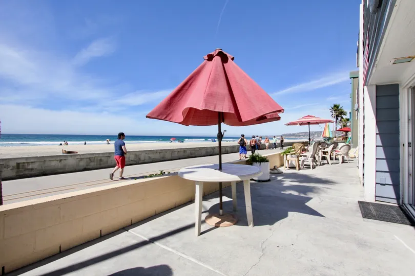 A sunny day in Mission Beach with people outdoors with umbrella-covered tables.