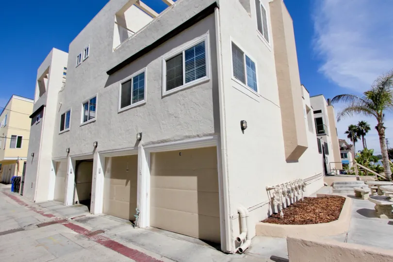 Three story gray building next to dirt planter under a blue sky at Mission Beach Villas in Mission Beach Ca