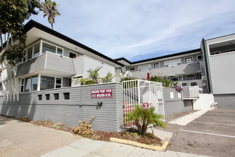The exterior of the blue Mission View Point apartment complex with off-street parking and a privacy fence.