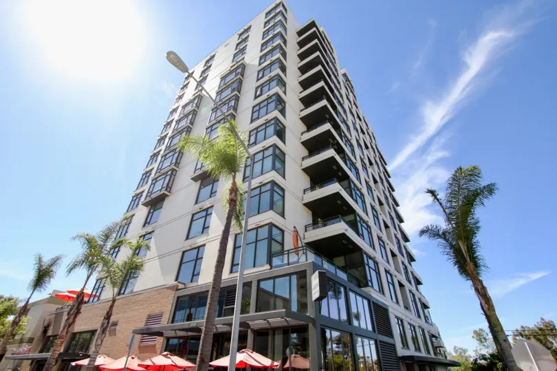 A tall building in a corner with some palm trees around it during a sunny day in Alicante, Mission Hills, CA