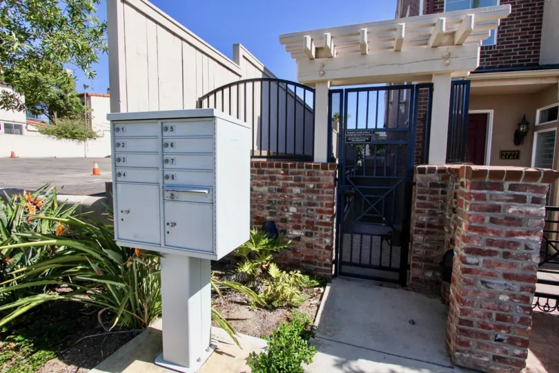 The entrance to a house with a mailbox and some bushes on front during a sunny day in Cambridge Square, Mission Hills, CA