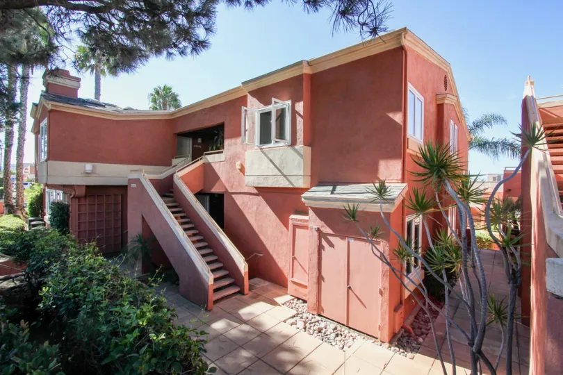 A dark pink two-story house with some trees and bushes surounding it during a sunny day in Columbia Crest, Mission Hills, CA