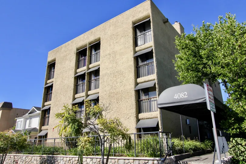 A blocky apartment building with some trees and bushes suround it during a sunny day in Cresthill Plaza, Mission Hills, CA
