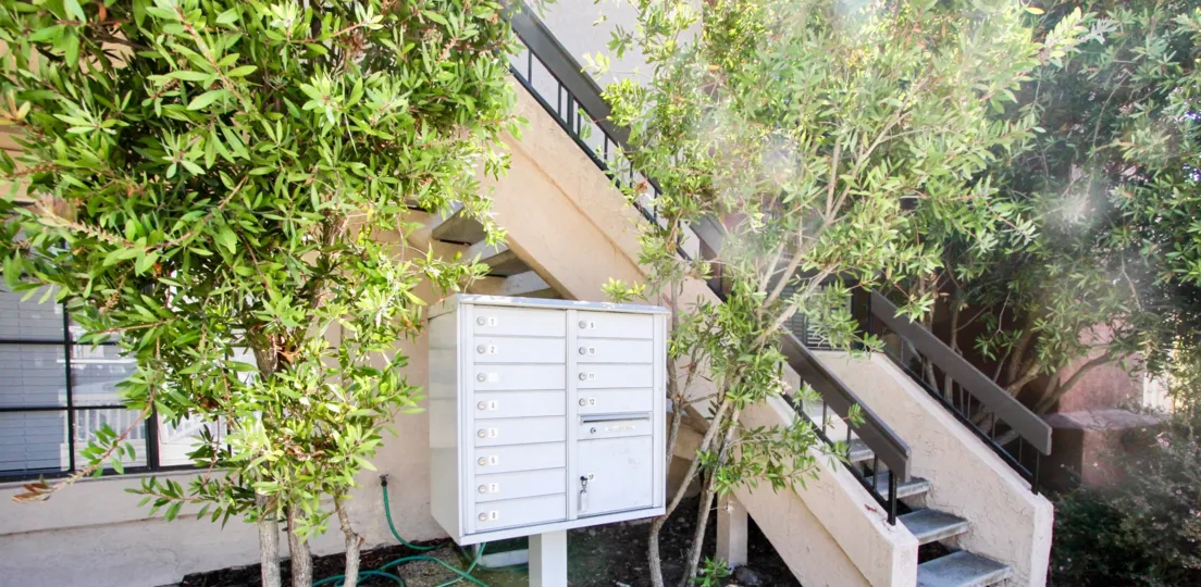 Long horizontal mailboxes sit in a silver box in front of a tan residential building at the El Roasl residential community