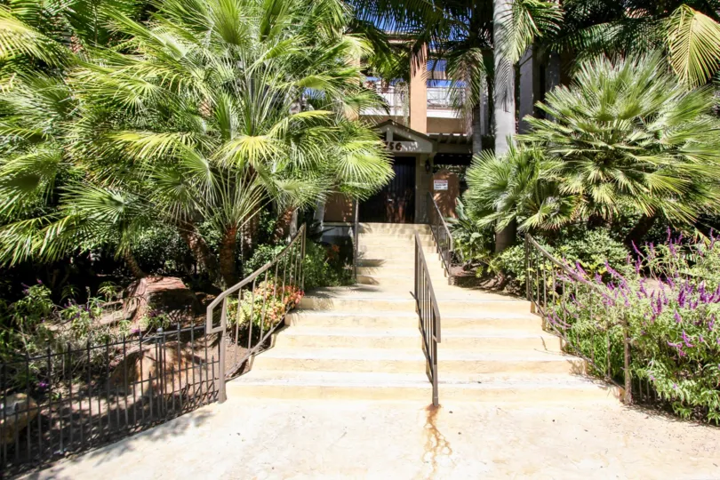 The plants with flowers and trees are covered the stairs of the pathway to the entrance in Essex Place