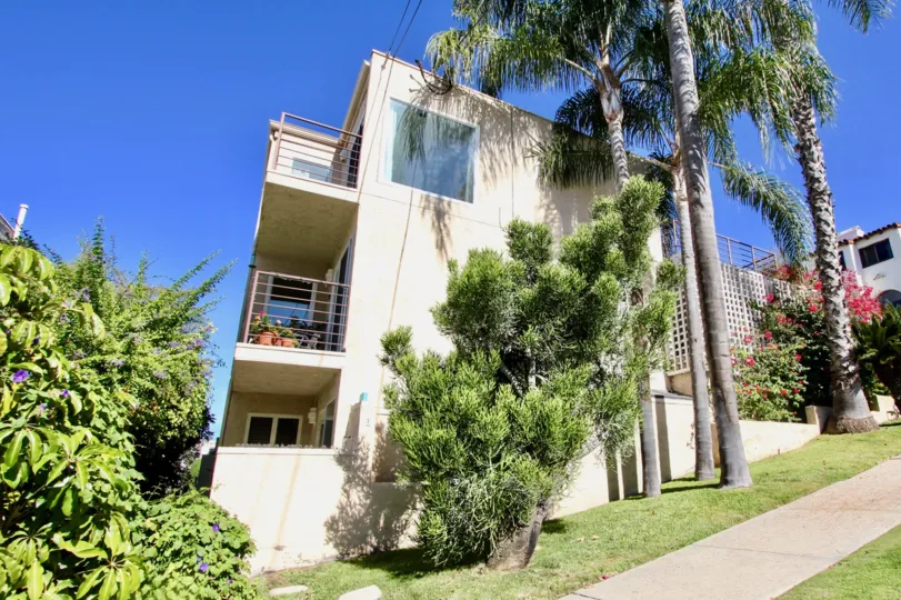 3 Story condominium building Mission Hills, California, with two decks, flanked with palm trees on a sunny day.