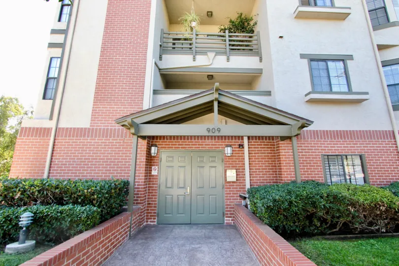 The entrance to an apartment building with brick exterior and some bushes to the sides during a sunny day in Sutter Canyon, Mission Hills, CA