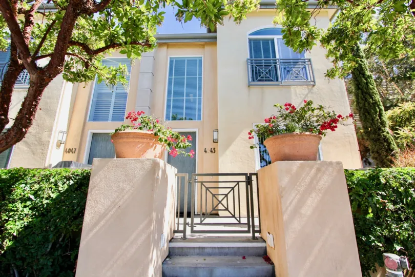 The entrance to a luxury house with some bushes and trees surounding it during a sunny day in Wellington Square, Mission Hills, CA
