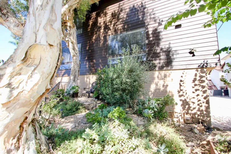 The side of a house with wooden exterior and some bushes and trees during a sunny day in West Walnut, Mission Hills, CA