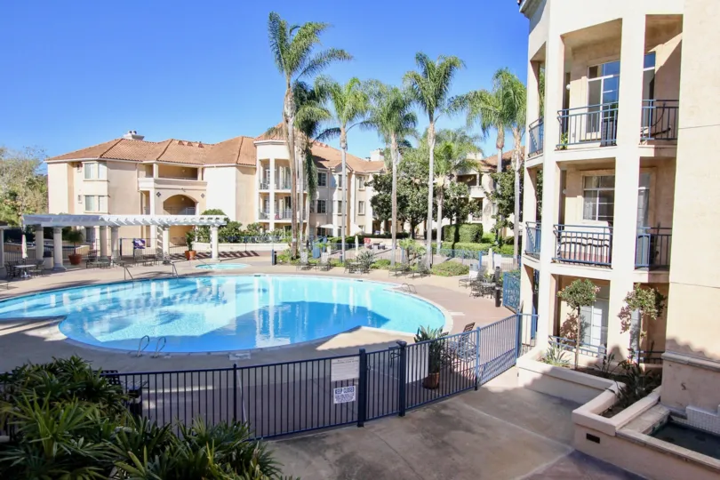 A sunny day poolside in the area of River Scene, fence, condo. chairs, table, palm trees