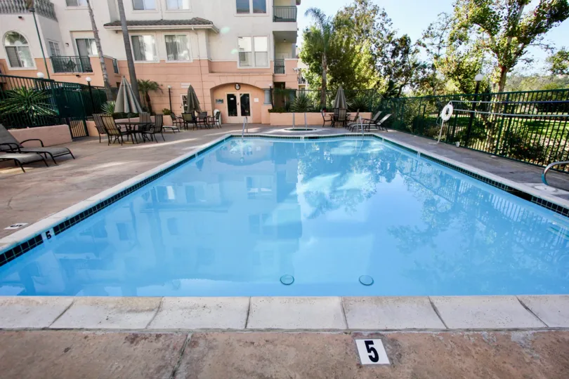 A 5' Deep, sunny inground pool patio area with umbrellas and seating for recreation in River Scene Mission Valley, California.