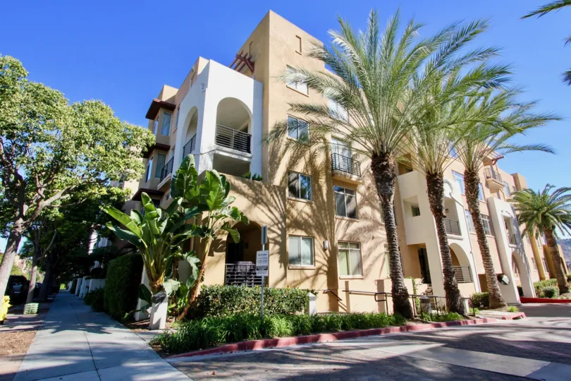 Building of the corner view of The Lido community in Mission Valley, CA. Contains palm trees and plants during the daytime. Sunny weather.