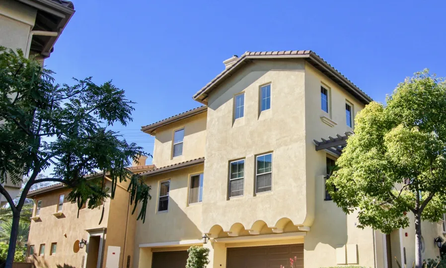 The exterior view of a tan stucco condo dwelling with private garage and trees at Verandas at Escala.