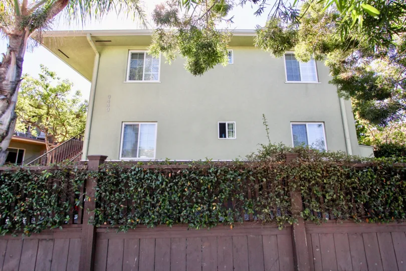 House with fence in the foreground, four windows, and trees all around