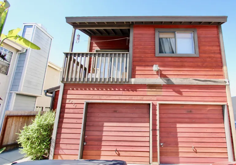 An exterior view of the rear of the charming Casa Heights condo complex showing two private storage units and private balcony under a blue sky.