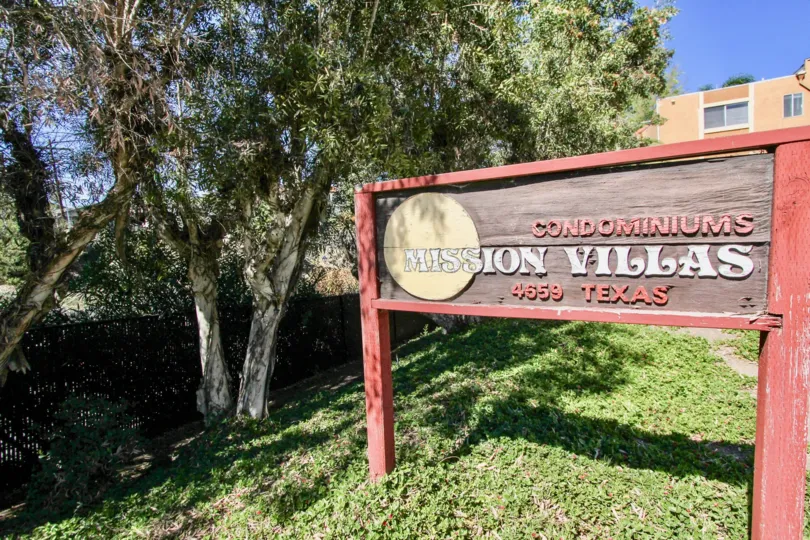 A sunny day in the area of Mission Villas, outside, welcome sign, trees, comdos, grass
