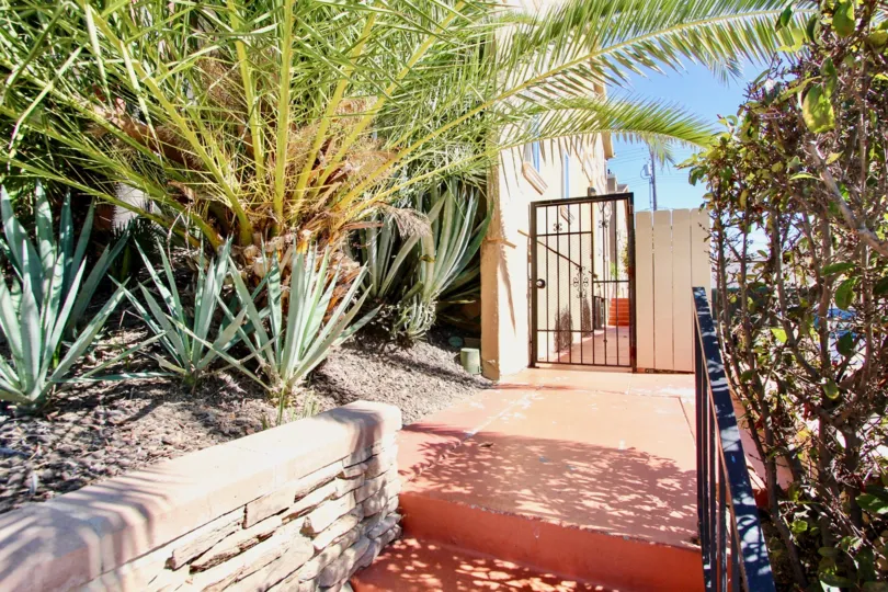 A sunny day in the area of Monroe Villas II, outside, entrance gate, bushes, wooden fence, brick stairs