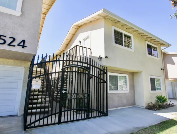 The exterior of the white stucco units at The Bently apartments with a black privacy gate.