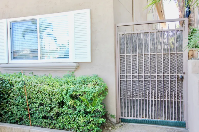 A light pink screen door next to a window and above hedges inside Utah West Villas in Normal Heights CA