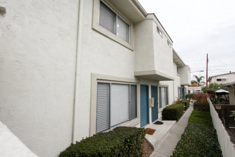 Walkway of an apartment building in Casa Diego II, North Park, California showing entrances and windows of individual units and shrubbery.