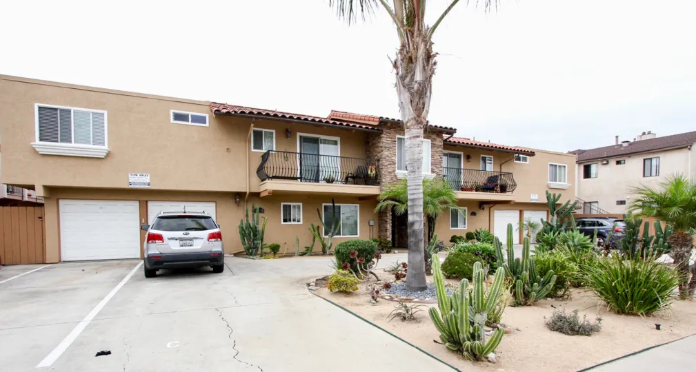 Apartment building with garage, balcony and palm tree and cacti out front