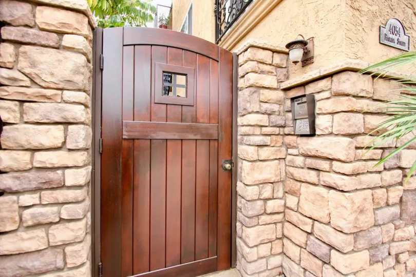 The outside private entrance at Florida Terrace with a call box, wooden gate, and stone wall.