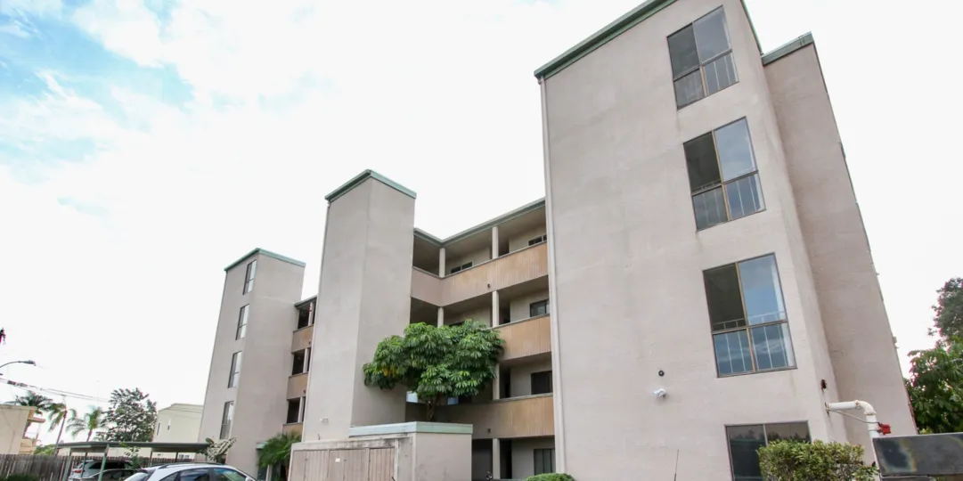 A parking lot is in front of a modern four story residential building in the Laurel Manor Community in North Park California
