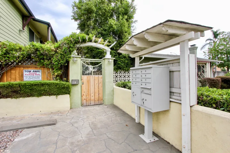 A gray metal mailbox sits under an awning near a gravel parking lot outside of an olive green apartment building in the Magnolia Walk community in North Park California