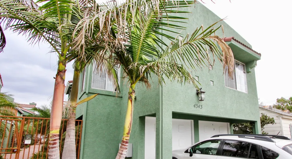 Green villa with a double garage, a fence and palm trees in the Majestic Palms Community in North Park, California