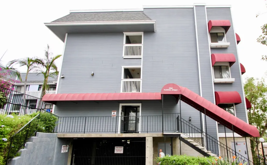 The exterior of a hotel in North Park, California in the Parkside Community. Weather is fair and the exterior of the hotel is gray and red.