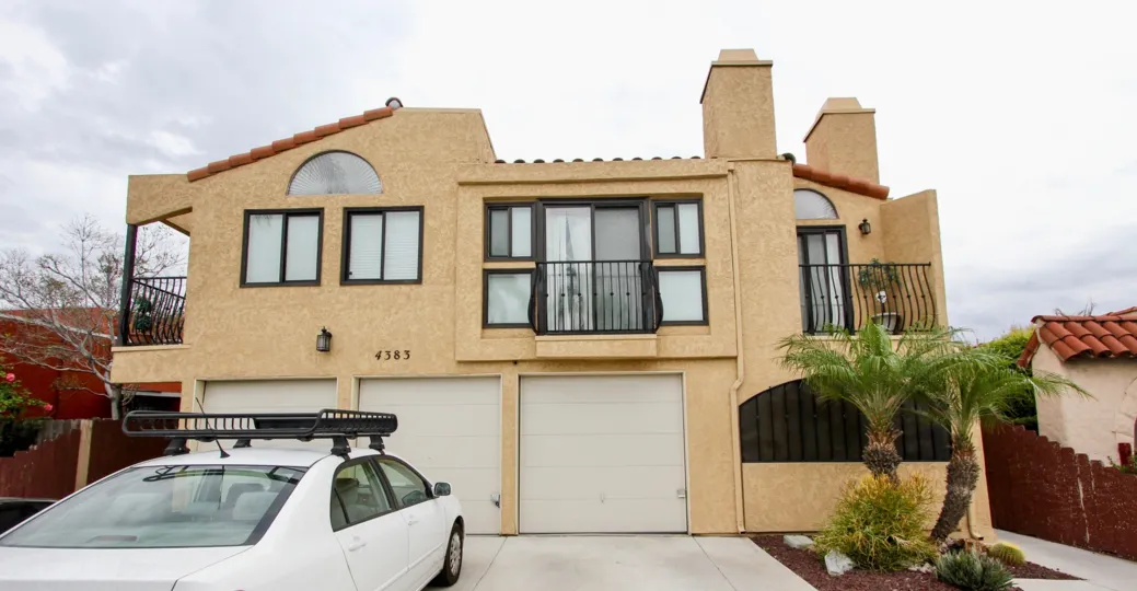 A cloudy day outside a beautiful home with a compact car and palm trees.