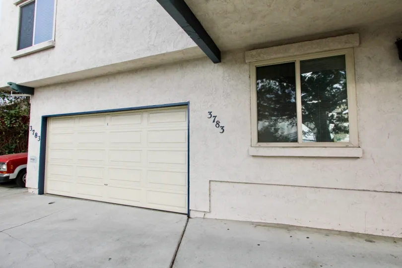 side of a beige mottled apartment building with a two car garage in the Swift Home community in North Park CaliforniaA red truck is parked on the