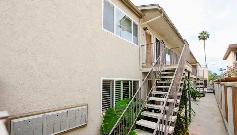 A set of stairs on the side of a beige building leads to an apartment door on the second floor of an apartment in The Garden District community of North Park California
