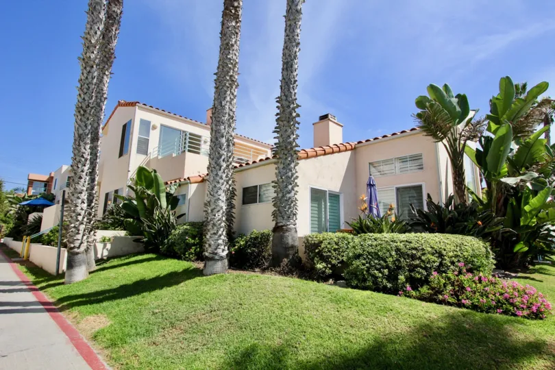 The sunny yard in front of Bermuda 12 with shrubs, flowers, palm trees, and an umbrella.