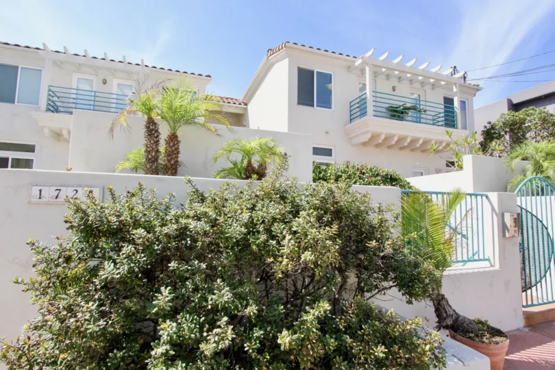 Ocean Front Condo in Ocean Beach CA, showing the frontage of the white colored condo with the gate and a few trees on a sunny day