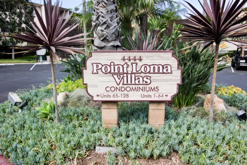 The Sign of Point Loma Villas Condominium with a small garden and a jeep in the backgroound