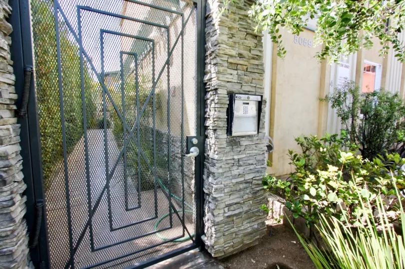 A sunny day at The Beach House, in front of the community gate with an intercom system and near a garden.