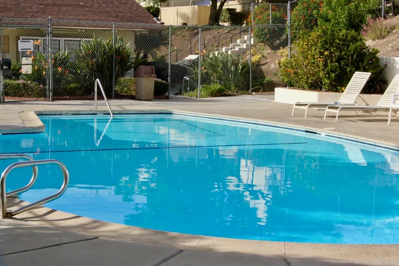Large gated pool next to a house, with pool chairs, located in El Camino Club Estates, Oceanside, California.