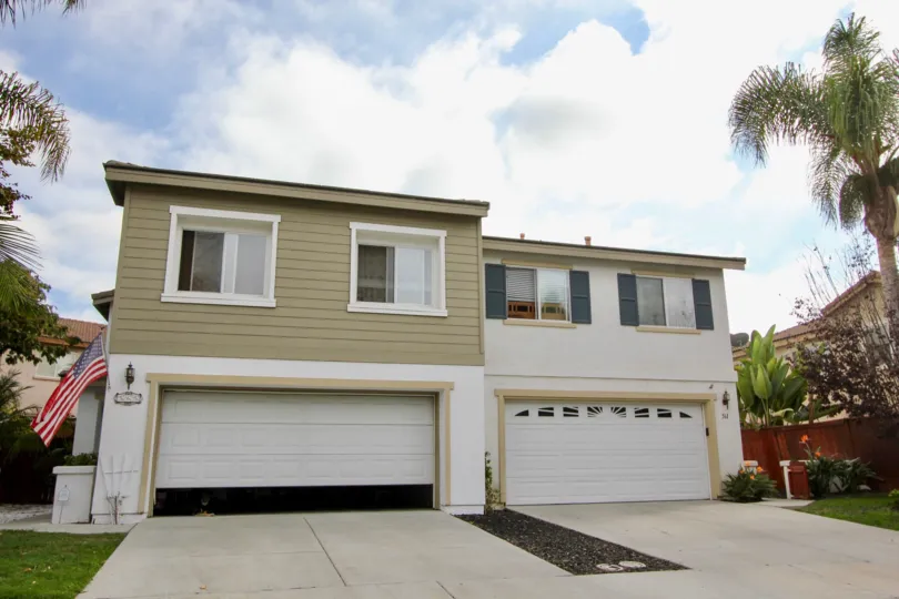 Large white home with white and beige and trees with a two car garage.