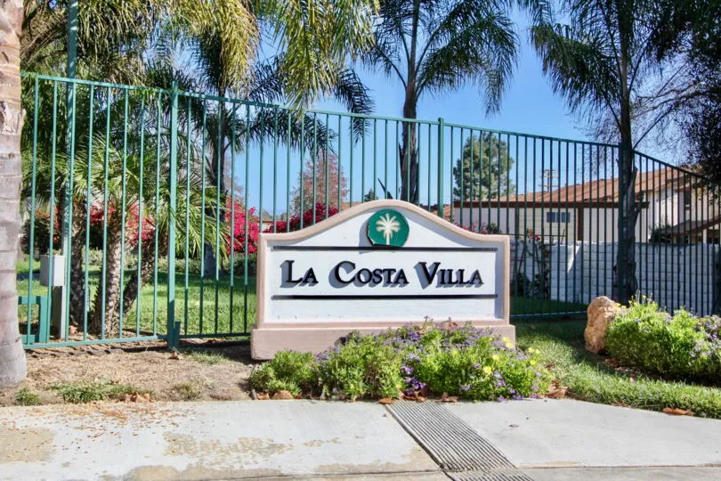 A sign in front of a fence by palm trees at La Costa Villa in Oceanside, CA