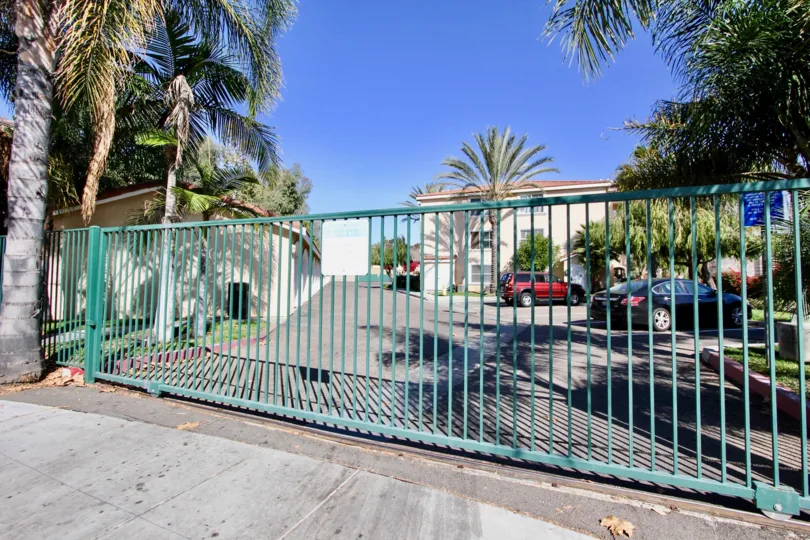 Secure gated road way entrance with ample visitor parking with large mature trees at La Costa Villas
