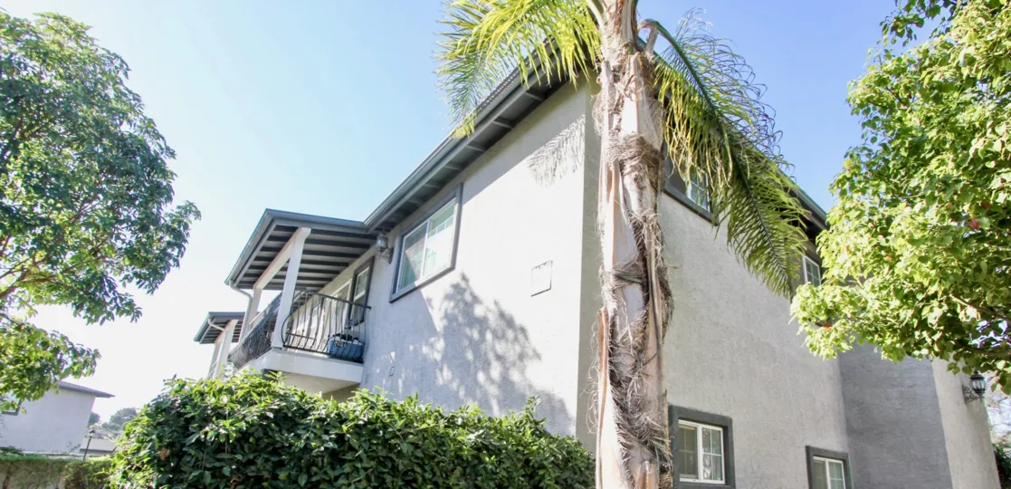 Two story gray building behind palms and trees in Oceanside CA at Las Brisas