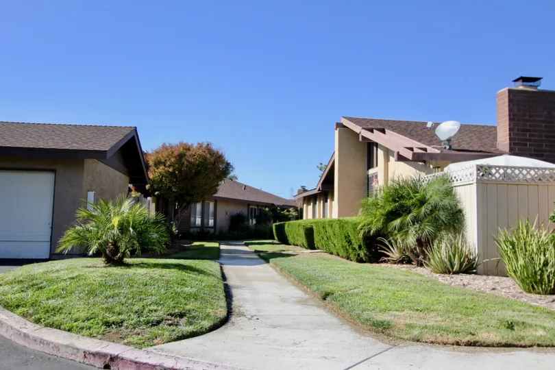 A sunny day in Los Arbolitos with green grasses, plants, and house garages