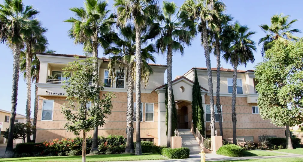 The exterior of an apartment unit at Neptune Point with exterior staircase and palm trees on a clear day.