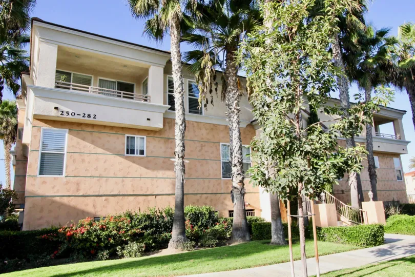 Sidewalk view of lawn and trees in front of the two-story condos at Neptune Point in Oceanside, CA