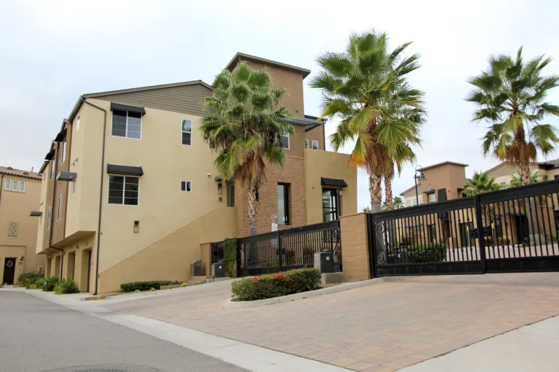 Minimalist beige and brown exterior condominiums in gated community surrounded by palm trees.
