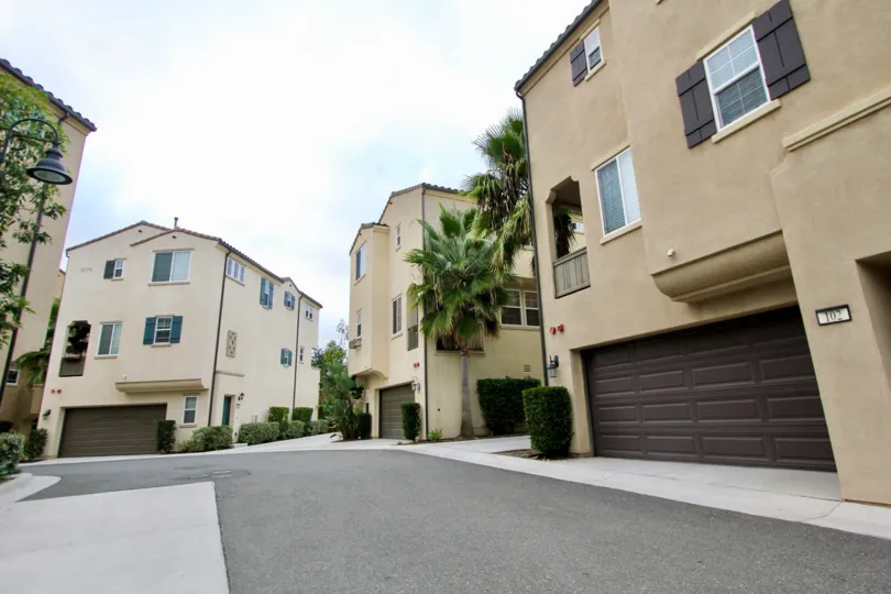 Beautiful sunny day streets of North River Village with beige walls, palm trees, and attached garages.